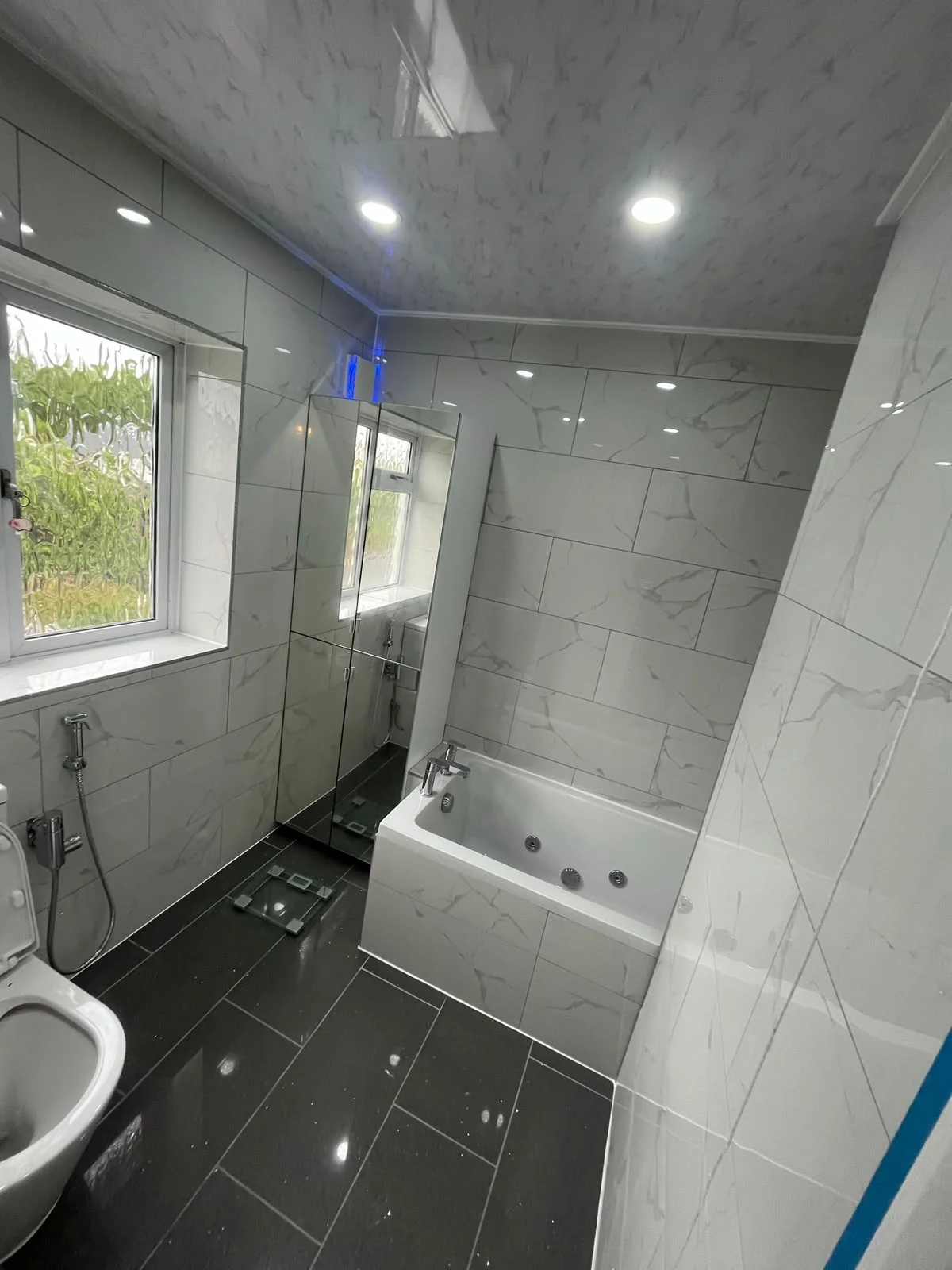 Spa bath with marble-effect wall tiles and black tiled floor — RV Renovation, Oxford